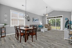 A spacious living room with a dining area, large windows, and a ceiling fan. - Barefoot Resort - Wedgewood #231 (North Myrtle Beach)