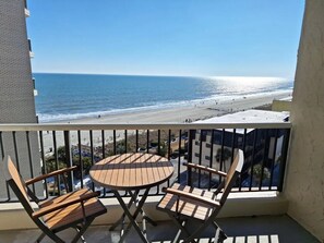Un balcon avec une table et des chaises donnant sur une plage.