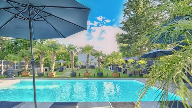 Ein Swimmingpool mit Liegestühlen und Sonnenschirmen, umgeben von Palmen und einem Zaun.