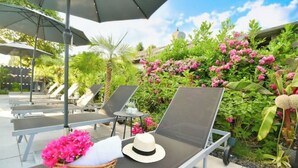 Ein Poolbereich mit Liegestühlen, einem Sonnenschirm und einem Korbwicker-Korb mit rosa Blumen.