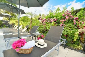 A poolside area with lounge chairs, a sun umbrella, and a wicker basket with pink flowers. - Adina vacation apartment (Teltow)