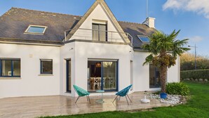 Een modern huis met twee verdiepingen, een schuin dak, grote ramen en een overdekte patio met buitenmeubilair.