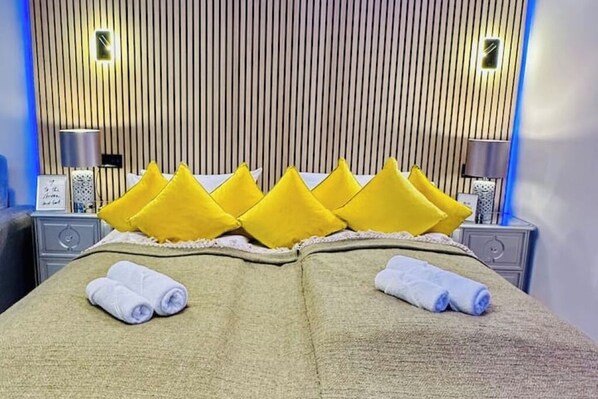 Quarto de hotel com uma cama, almofadas amarelas e toalhas dobradas.