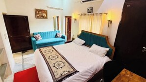 A hotel room with a bed, a blue sofa, a wooden nightstand, and a wall-mounted air conditioner. - Brightness in the Sky – A Cozy, Peaceful Stay with Modern Comforts (Jaipur)