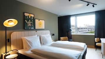 Habitación de hotel con cama, dos sillas, escritorio, lámpara y cuadros en la pared.