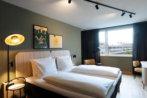 A hotel room with a bed, two chairs, a desk, a lamp, and artwork on the wall. - Scandic Charlottenburg (Berlin)