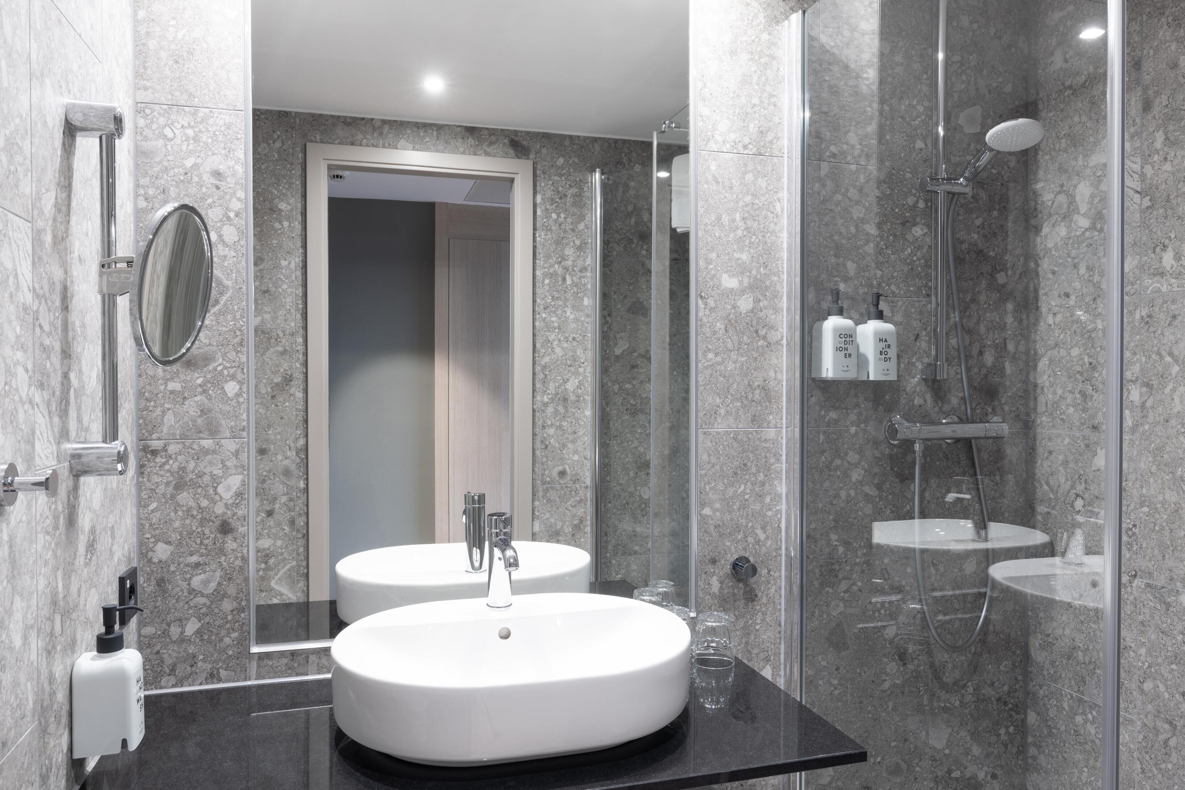 Un baño moderno con dos lavamanos, un espejo y una zona de ducha.