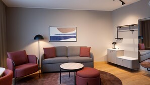 Una sala de estar moderna con un sofá gris, sillones rojos, una mesita redonda y una lámpara de pie.