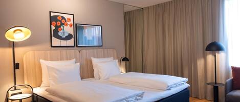 Habitación de hotel con cama doble, dos mesitas de noche, una lámpara de pie y una obra de arte en la pared.
