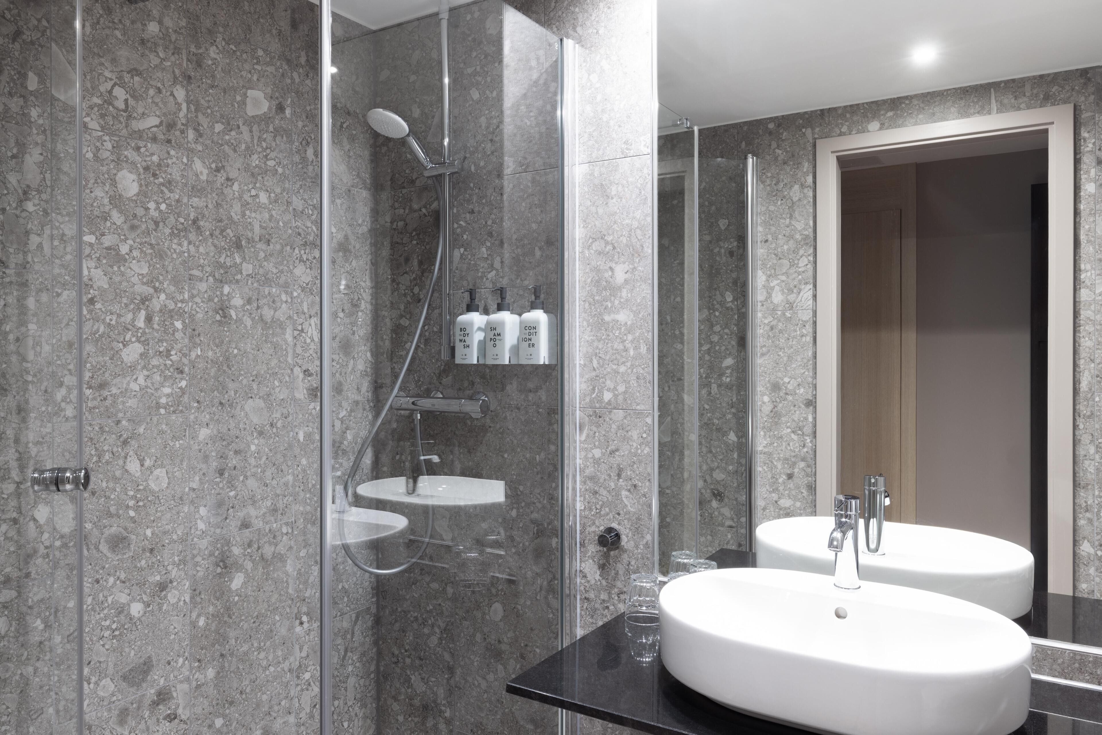 A modern bathroom with a glass-enclosed shower, two sinks, and toiletries on a shelf.