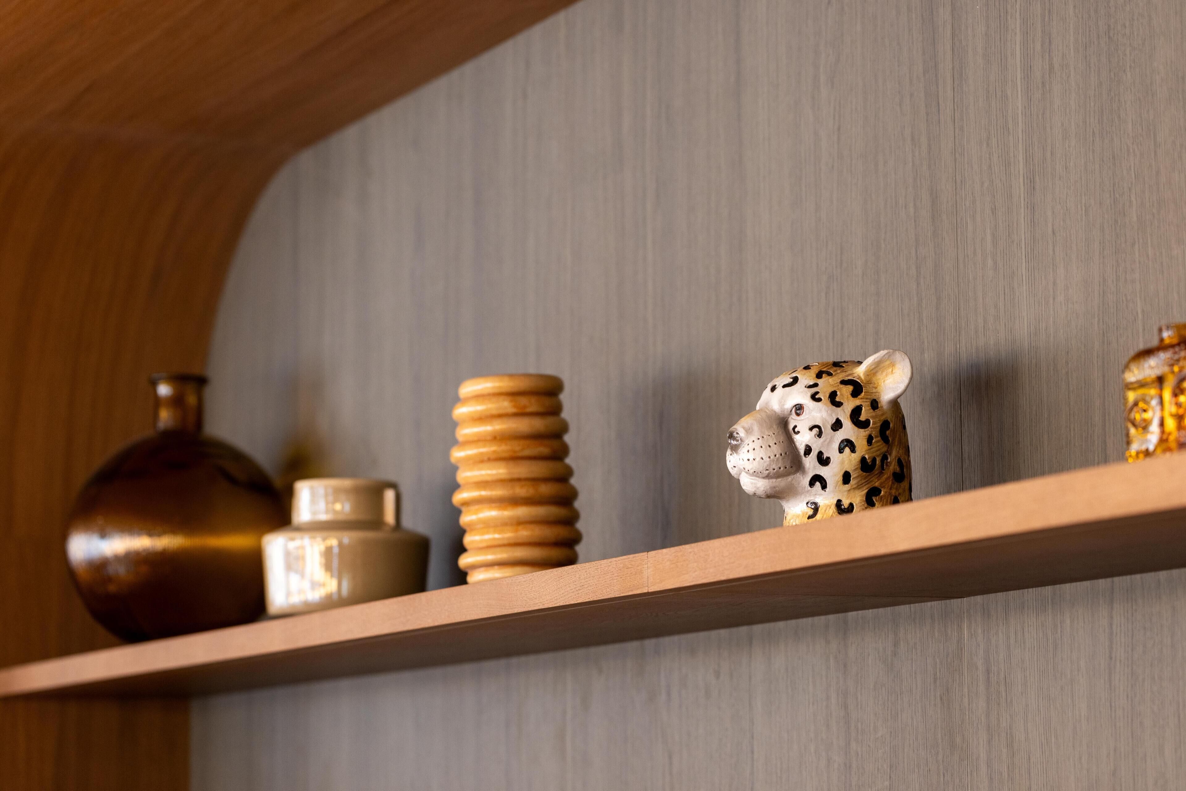 A shelf with a ceramic jug, stacked wooden bowls, and a leopard figurine.