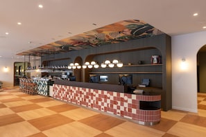 A bar area with a checkered floor, a counter with a patterned backsplash, and overhead lighting. - Scandic Charlottenburg (Berlin)