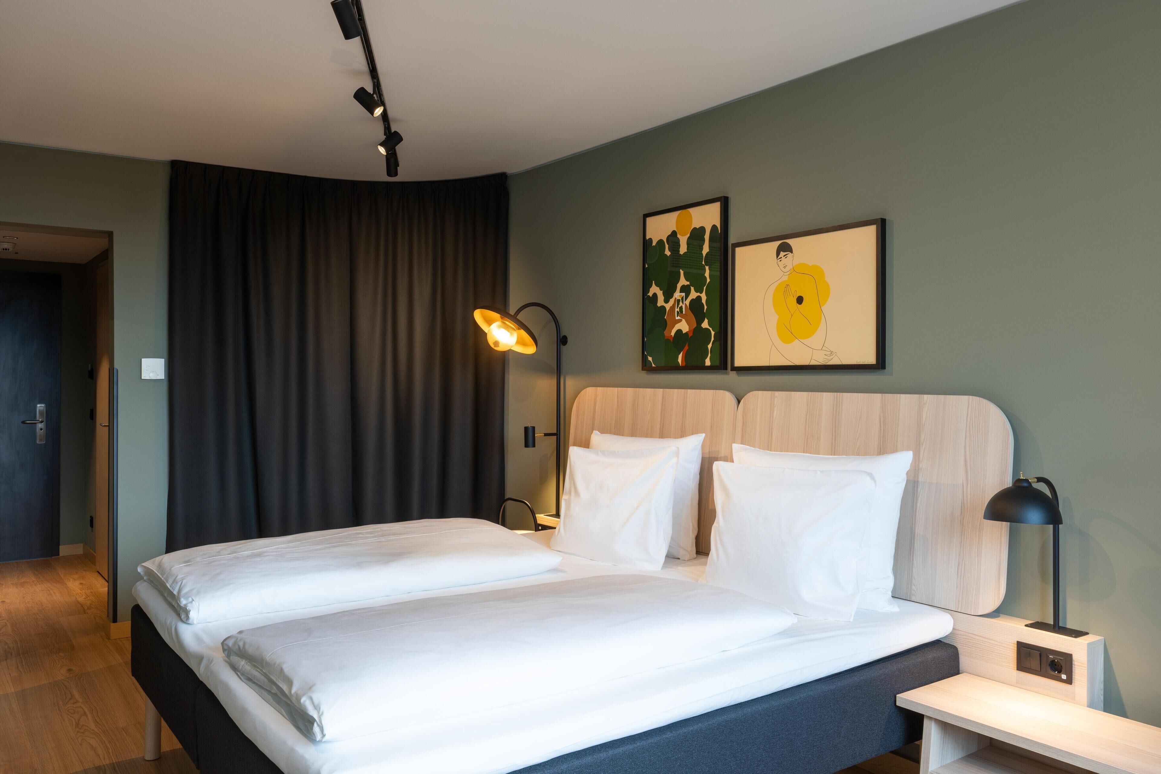 A hotel room with a bed, a nightstand, a lamp, and two wall art pieces.