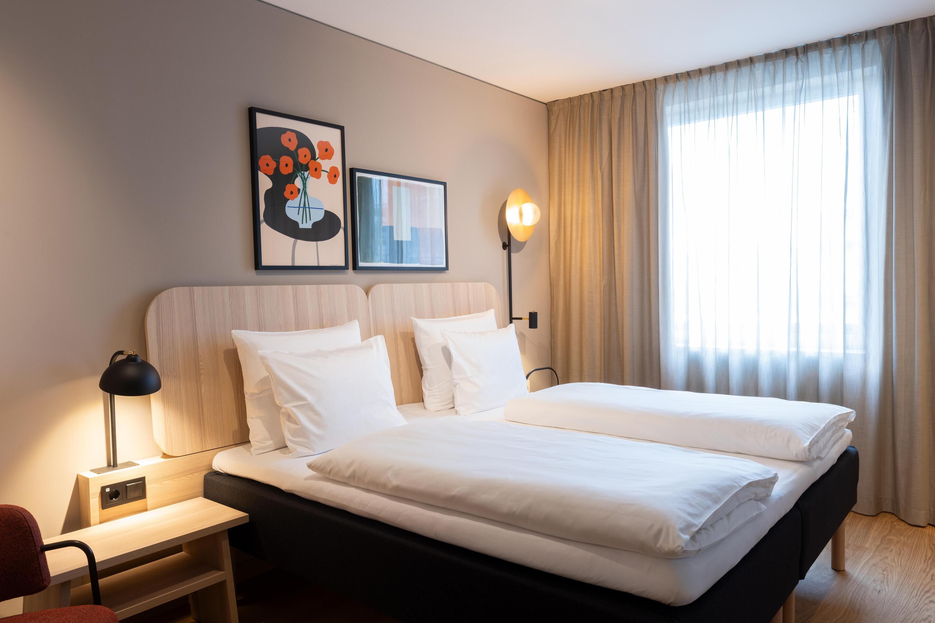 A hotel room with a large bed, two bedside tables, a chair, a desk, and a window with curtains.