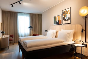 A hotel room with a large bed, two bedside tables, a desk, a chair, and a lamp. - Scandic Charlottenburg (Berlin)