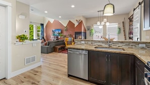 A modern kitchen with a dishwasher, a built-in oven, and a large island with a sink. - Casa Tierra | Walk to Old Town via Poudre Trail (Fort Collins)