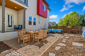 Eine Terrasse mit Tisch und Stühlen, eine Holzterrasse und ein rotes Gebäude im Hintergrund.