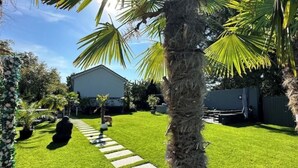 A well-maintained backyard with a lawn, a stone pathway, and a palm tree. - Vacation apartment Luna (Teltow)