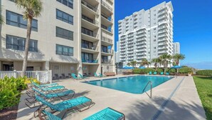A pool area with sun loungers and a view of high-rise buildings. - Arcadian Dunes 11 #343- 2BR- Pool, Hot Tub (Myrtle Beach)