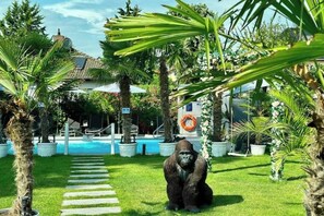 En gorilla statue i en frodig have med et bassin og en bygning i baggrunden.