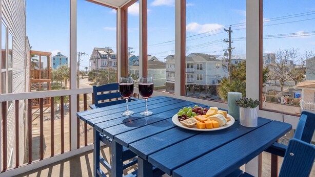A balcony with a table set for two, featuring a plate of cheese, grapes, and bread, and two glasses of red wine. - Ocean Edge 204- Cherry Grove 2BR- Pool (North Myrtle Beach)