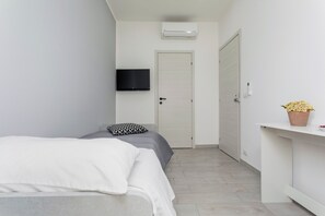 A bedroom with a bed, a TV mounted on the wall, a door, and a potted plant on a shelf.