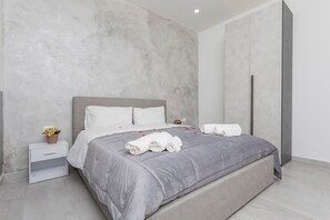 A modern bedroom with a grey bed, white pillows, and a nightstand with a plant. - Pm House – Double Room (Misterbianco)