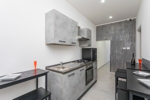 A modern kitchen with grey cabinets, a black stove, and a dining area with a black table and chairs. - Pm House – Double Room (Misterbianco)