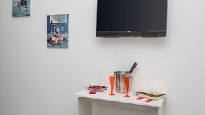 A room with a flat-screen TV mounted on the wall, a small table with a tray of candles, a book, and two glasses. - Pm House - Suite with Jacuzzi (Misterbianco)