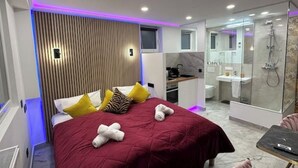 Una habitación de hotel moderna con una cama grande, un escritorio y un baño con ducha de vidrio.