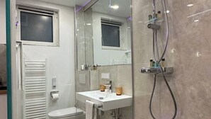 Un baño moderno con cabina de ducha de vidrio, un lavabo blanco y un inodoro.