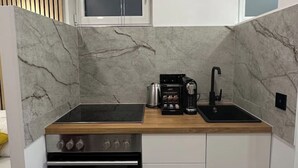 Una cocina compacta con estufa negra, cafetera y lavabo.