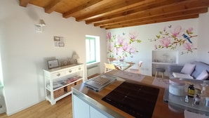 Une cuisine avec des poutres en bois, un coin repas avec une table en verre et un mur décoré de fresques représentant des motifs floraux et des oiseaux.