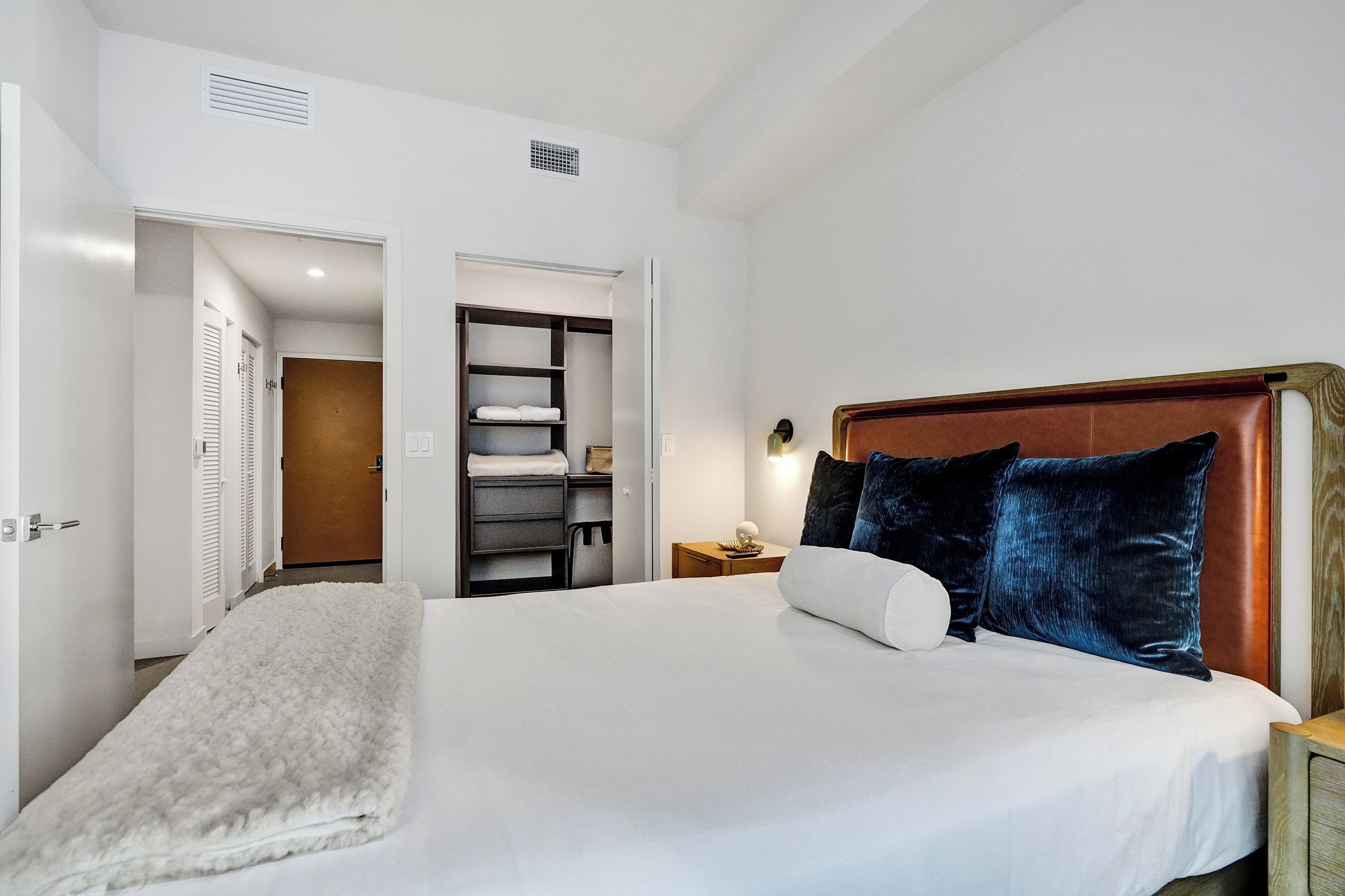 A bedroom with a large bed, a wooden headboard, a bedside table, and a walk-in closet with shelves and hanging space.