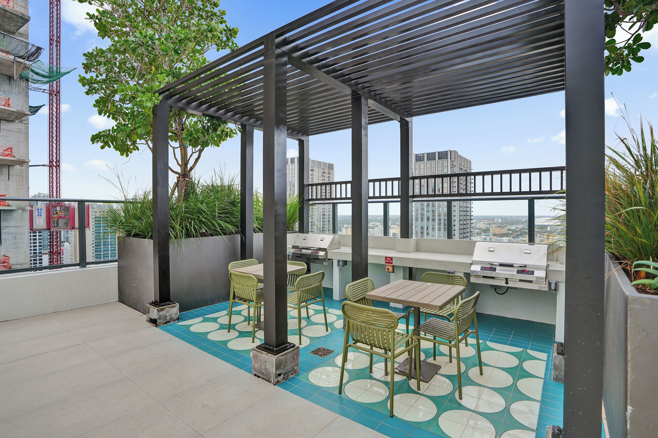 A rooftop terrace with a pergola, outdoor seating, a grill, and a view of the cityscape.