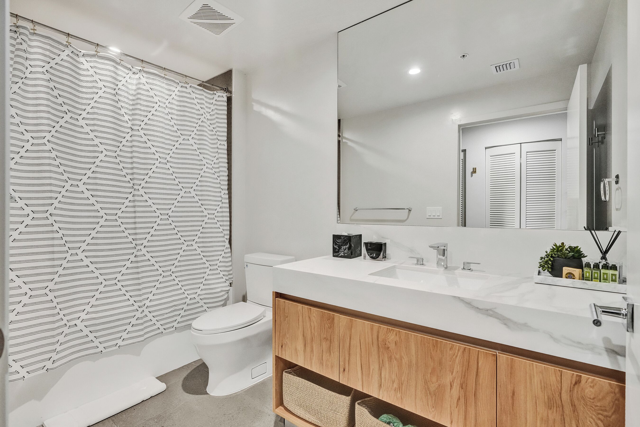 A modern bathroom with a white toilet, a large mirror, and a wooden vanity.