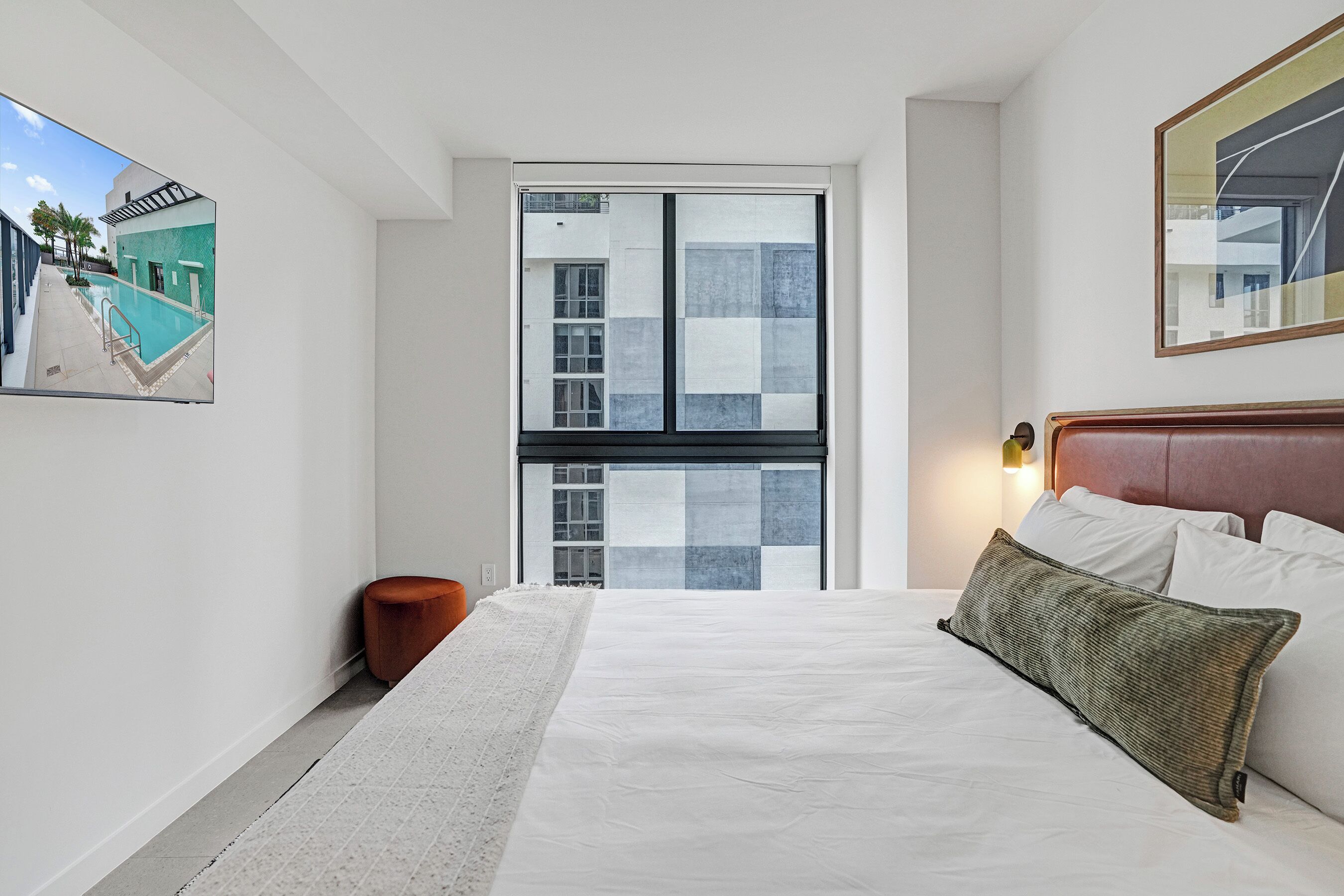 Een moderne hotelkamer met een groot bed, uitzicht op een zwembad en een ingelijst kunstwerk aan de wand.