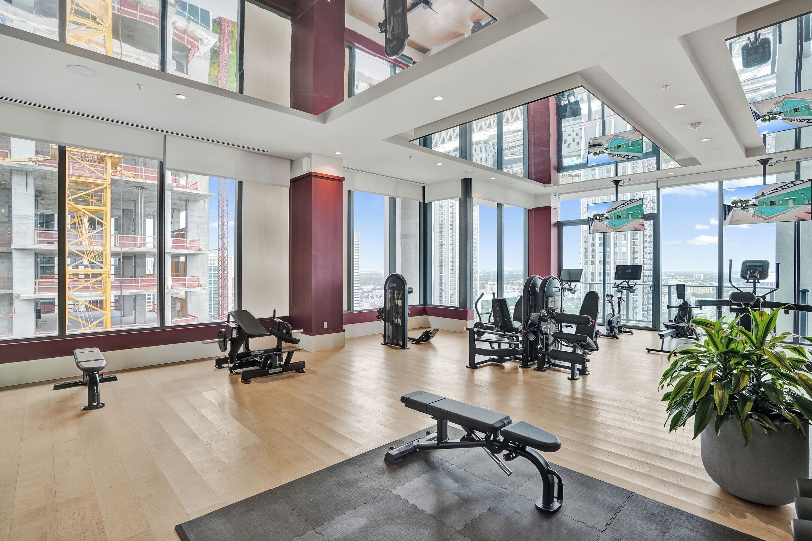 Une salle de sport spacieuse, dotée de divers équipements d’exercice, de grandes fenêtres offrant une vue sur la ville et d’un design architectural moderne.