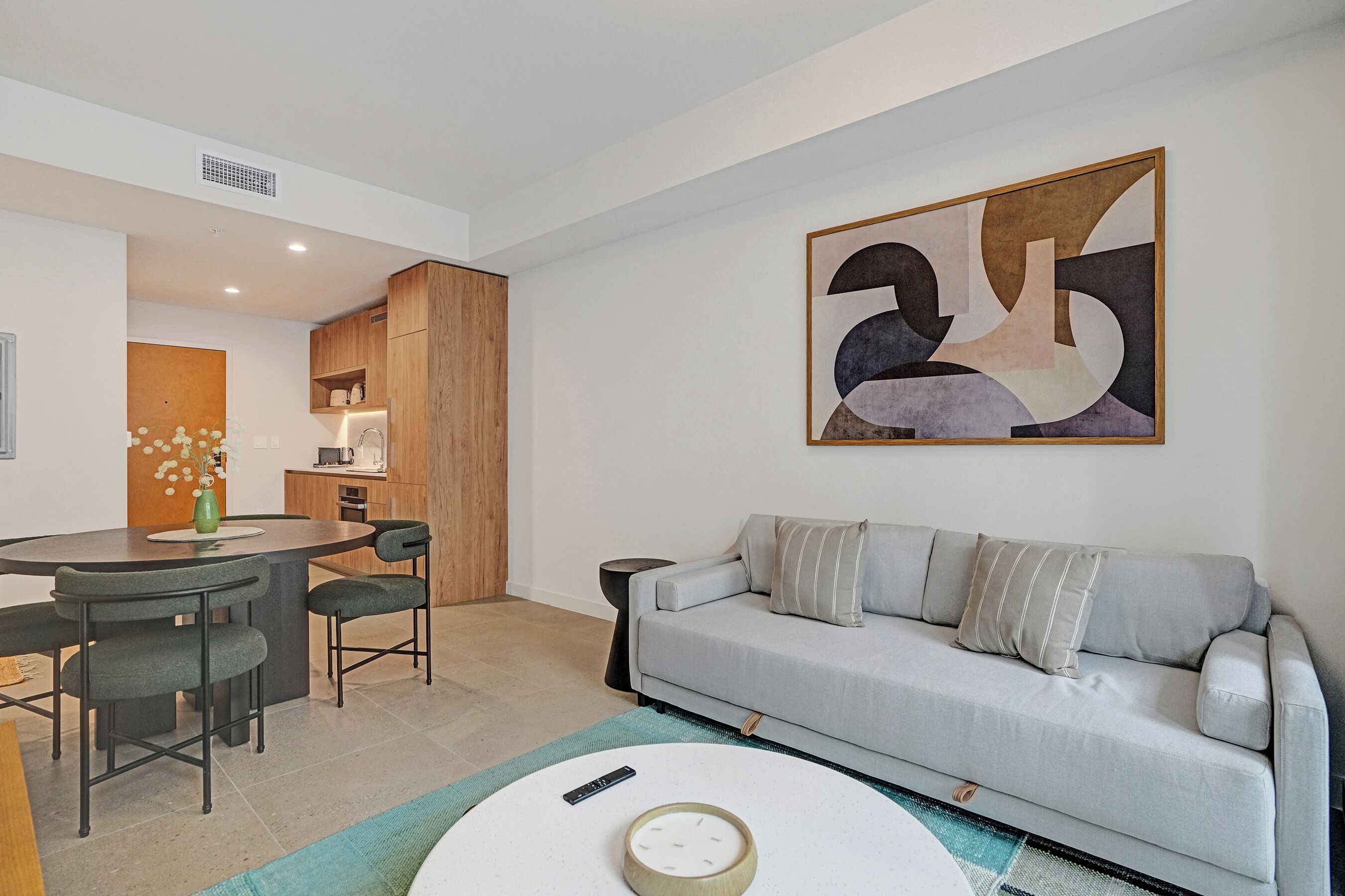 A modern living room with a grey sofa, a round coffee table, and a dining area with a wooden table and chairs.