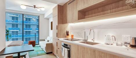 A modern kitchen with wooden cabinets, a white countertop, a built-in oven, and a large window with a view of buildings.