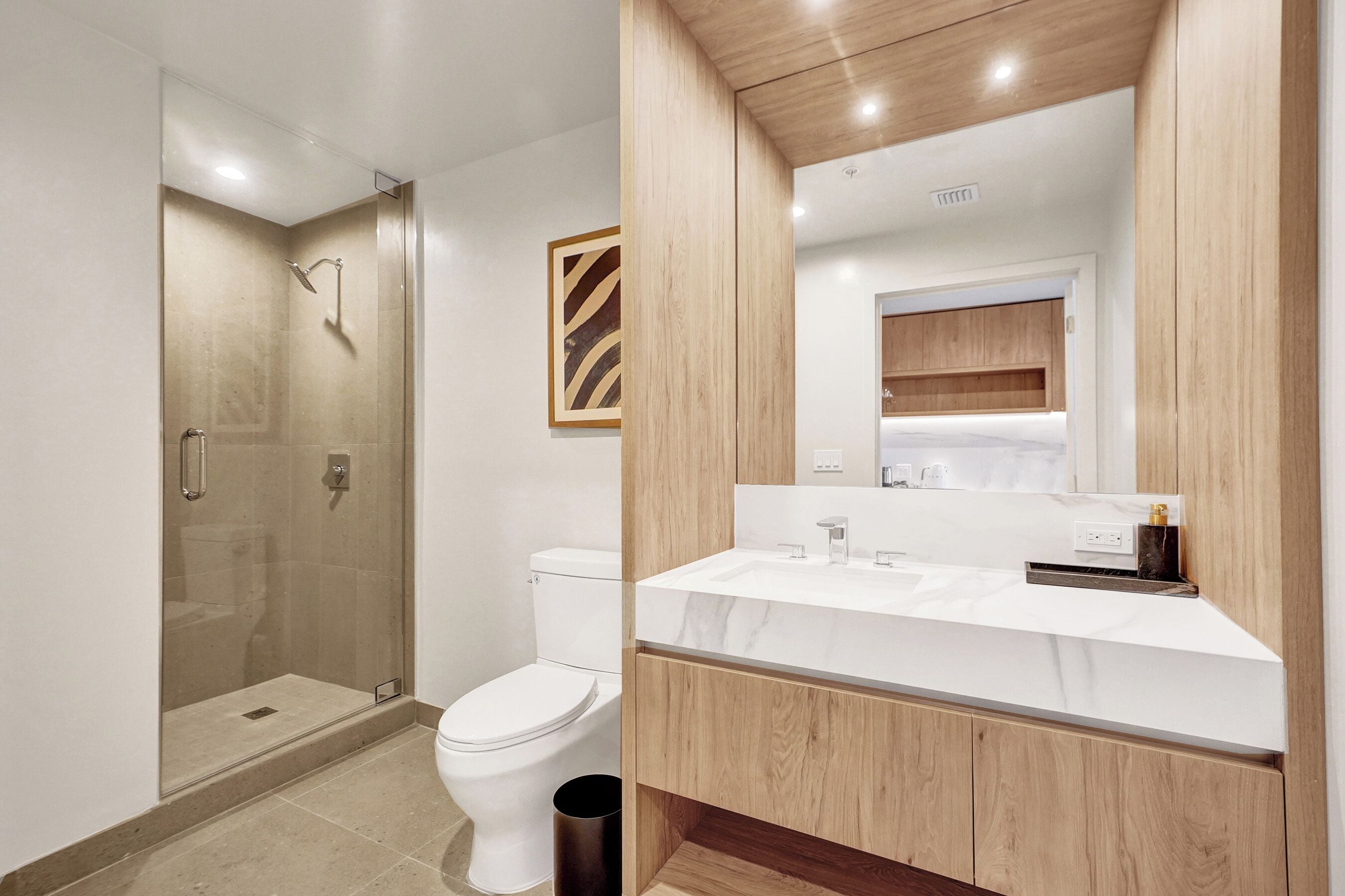 A modern bathroom with a glass shower enclosure, a white toilet, and a wooden vanity with a marble countertop.