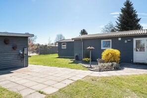 A residential property with a paved driveway, a small garden with yellow flowers, and a tall evergreen tree. - Cozy holiday home near the beach (Væggerløse)