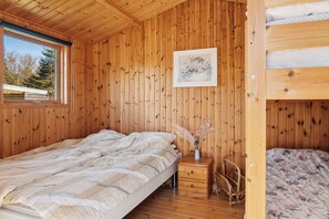 A wooden cabin bedroom with a bunk bed, a single bed, a nightstand, a chair, and a framed picture on the wall. - Cozy holiday home near the beach (Væggerløse)