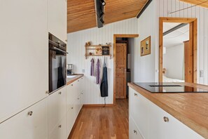 A kitchen with wooden cabinets, a black countertop, and a hanging rack with kitchen utensils. - Cozy holiday home near the beach (Væggerløse)