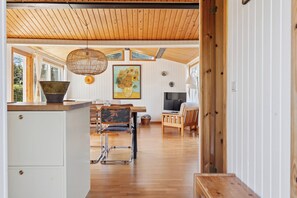 A spacious kitchen with wooden cabinets, a dining area with a table and chairs, and a television. - Cozy holiday home near the beach (Væggerløse)