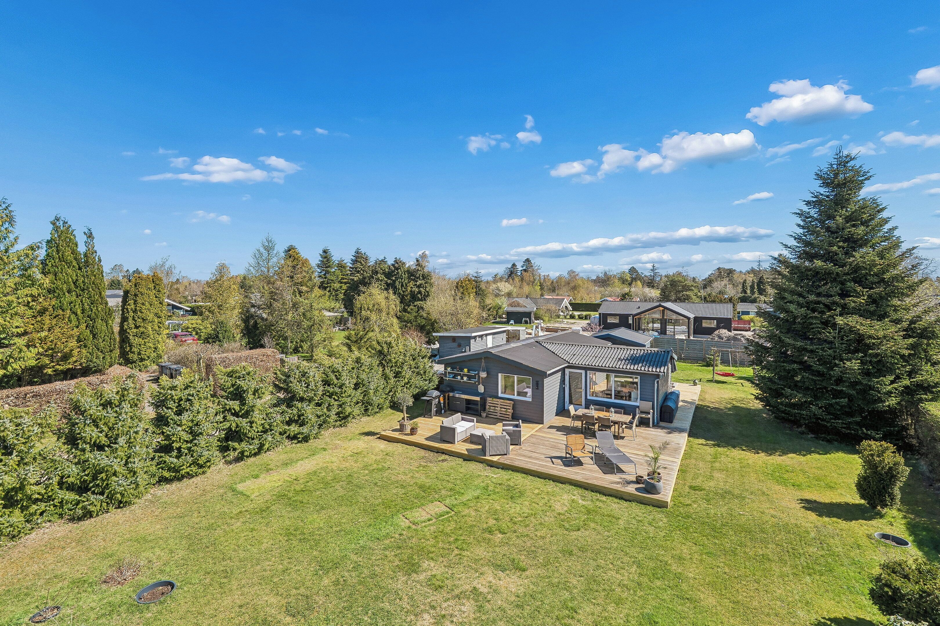 Une maison moderne dotée d’une grande terrasse, entourée d’arbres et offrant une vue sur un ciel dégagé.