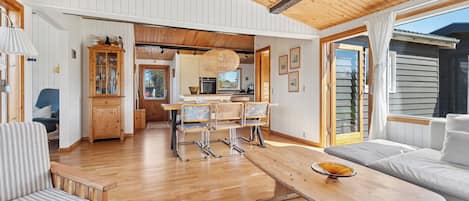 Un salón amplio con techo de madera, una mesa de comedor con sillas, un sofá y una cocina al fondo.