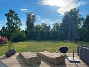 Une terrasse dotée de meubles en osier, d’un saladier noir et d’un parasol.