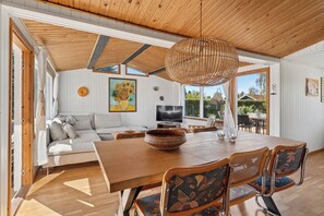 A modern living room with a wooden ceiling, a large dining table, a sofa, and a TV. - Cozy holiday home near the beach (Væggerløse)