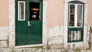 Eine grüne Tür mit der Nummer 12, ein kleines Fenster mit einem Ventilator und eine Steinsäule.